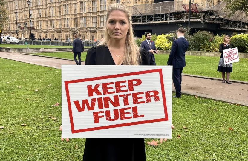 Harriet Cross holding a 'Keep Winter Fuel' sign outside Parliament in Westminster