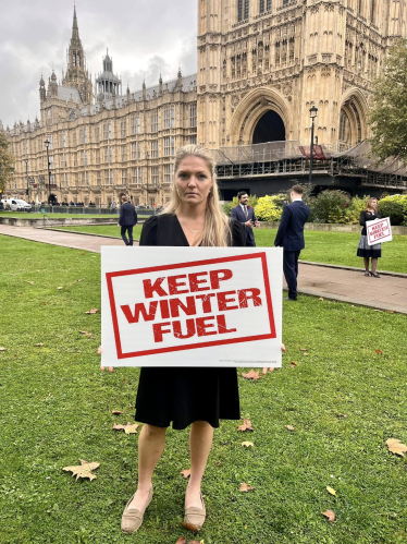 Harriet Cross holding a 'Keep Winter Fuel' sign outside Parliament in Westminster